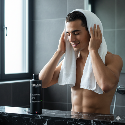 Man drying his hair with a towel in a bathroom, with a Norflake shampoo bottle on the counter.